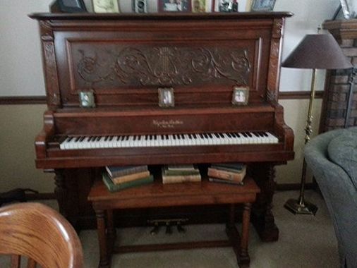 Antique wooden piano with carved details, books, and stool in a living room.