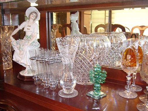 Display of crystal glassware and a porcelain figurine on a wood surface, reflected in a mirror.