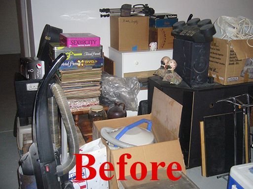 Messy storage area with boxes, objects, and a vacuum cleaner piled in front of a wall.