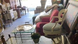 Sunlit vintage-style seating area with colorful chairs, glass tables, and decor items indoors.