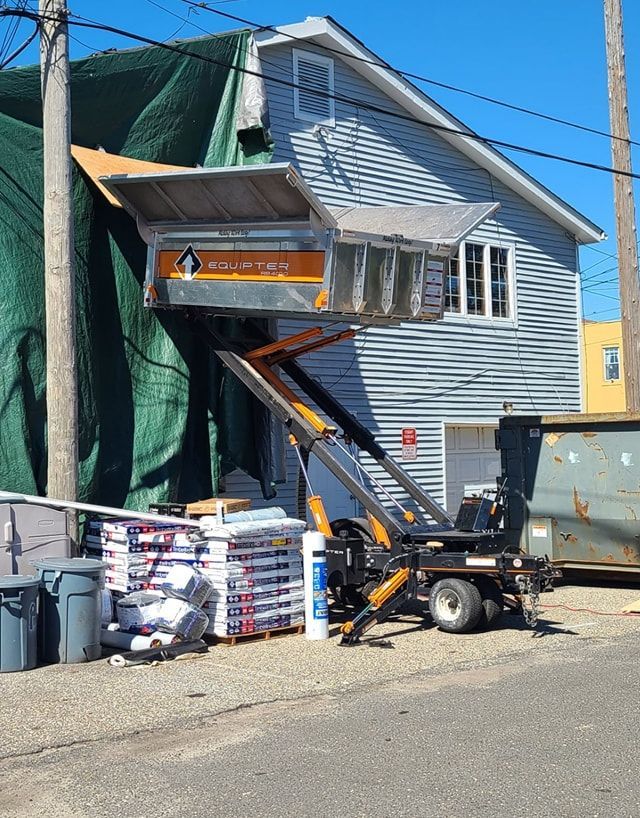 A house with a green tarp on it is being lifted by a lift.
