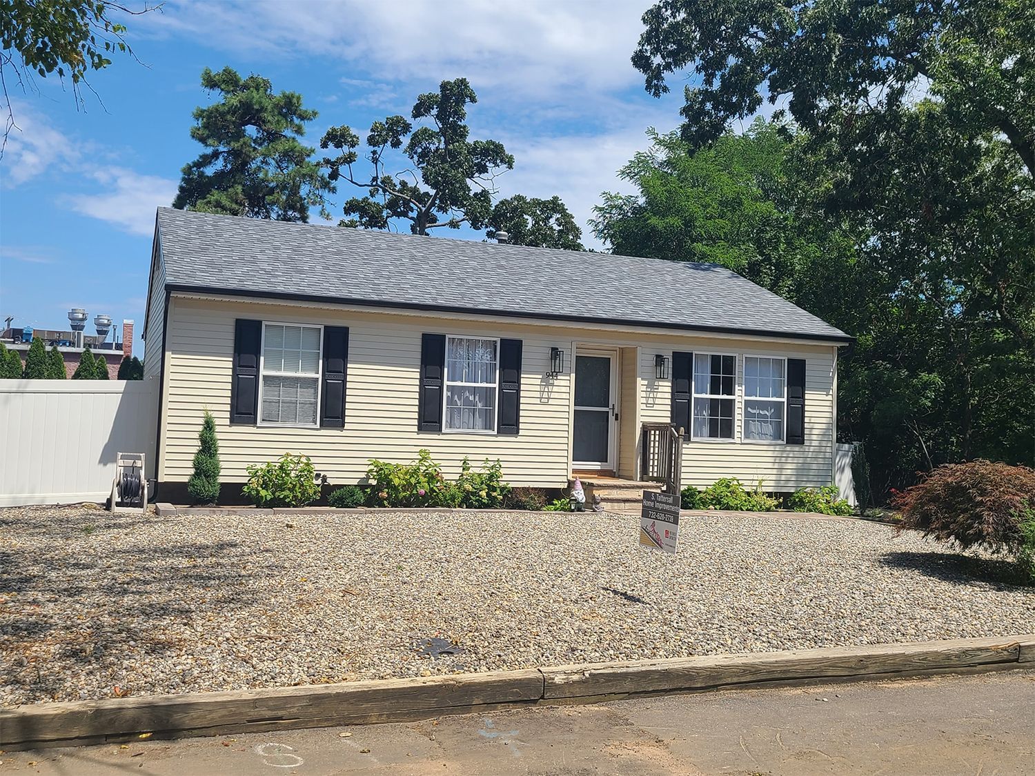 A white house with black shutters and a gravel driveway in front of it.