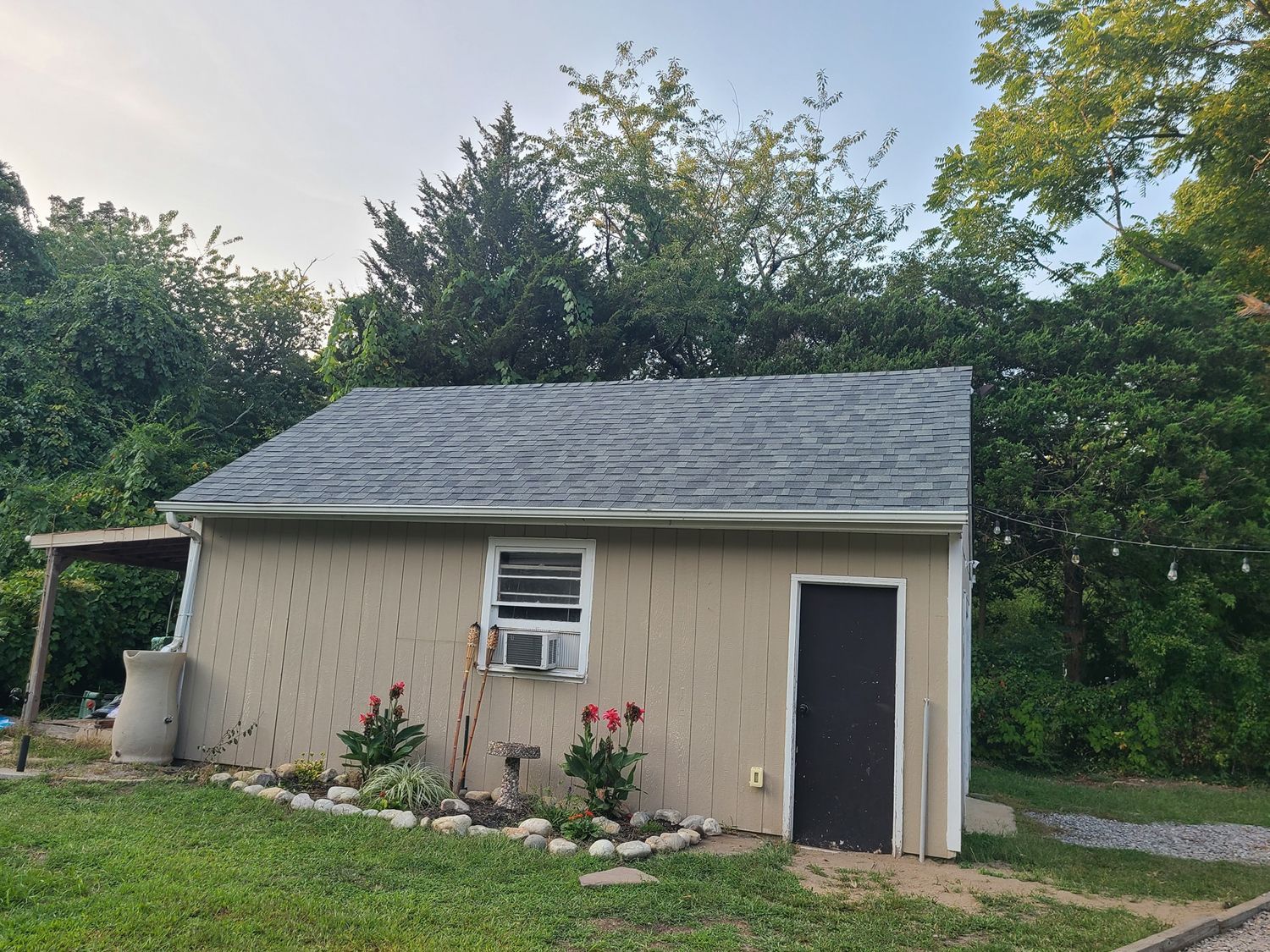 A small house with a slate roof is surrounded by trees.