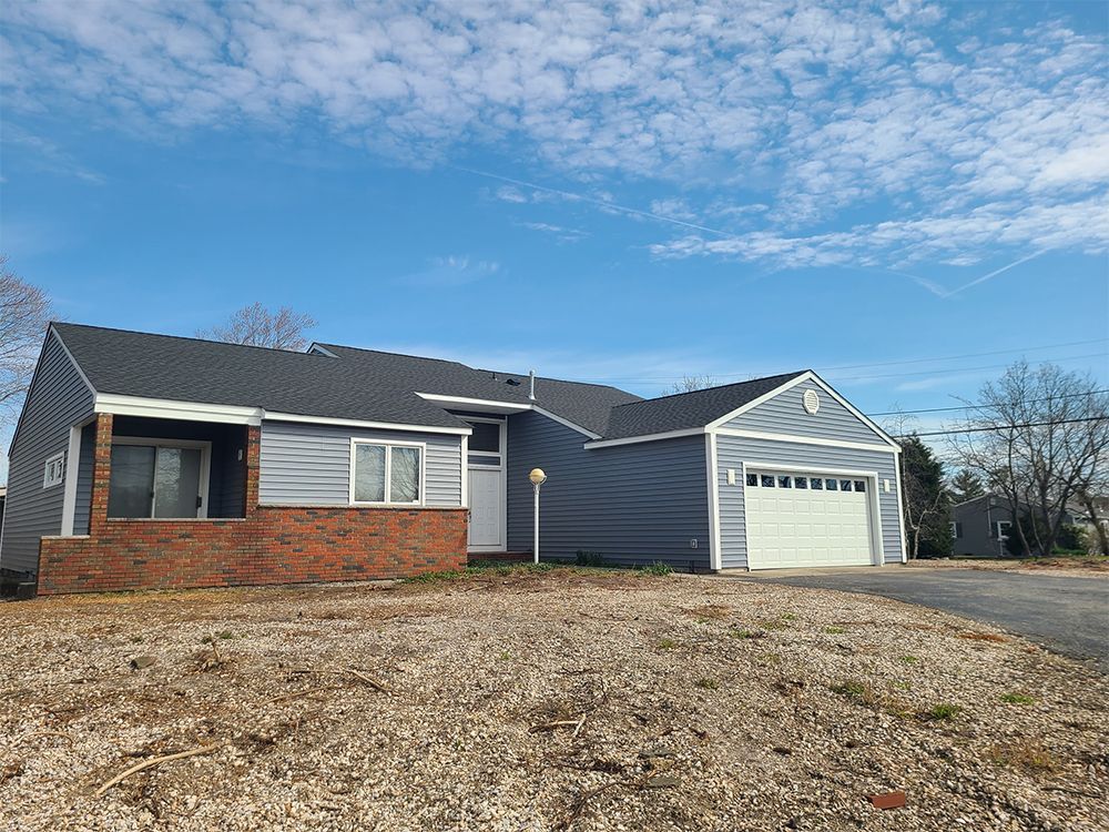 A house with a garage and a porch is sitting on top of a dirt field.