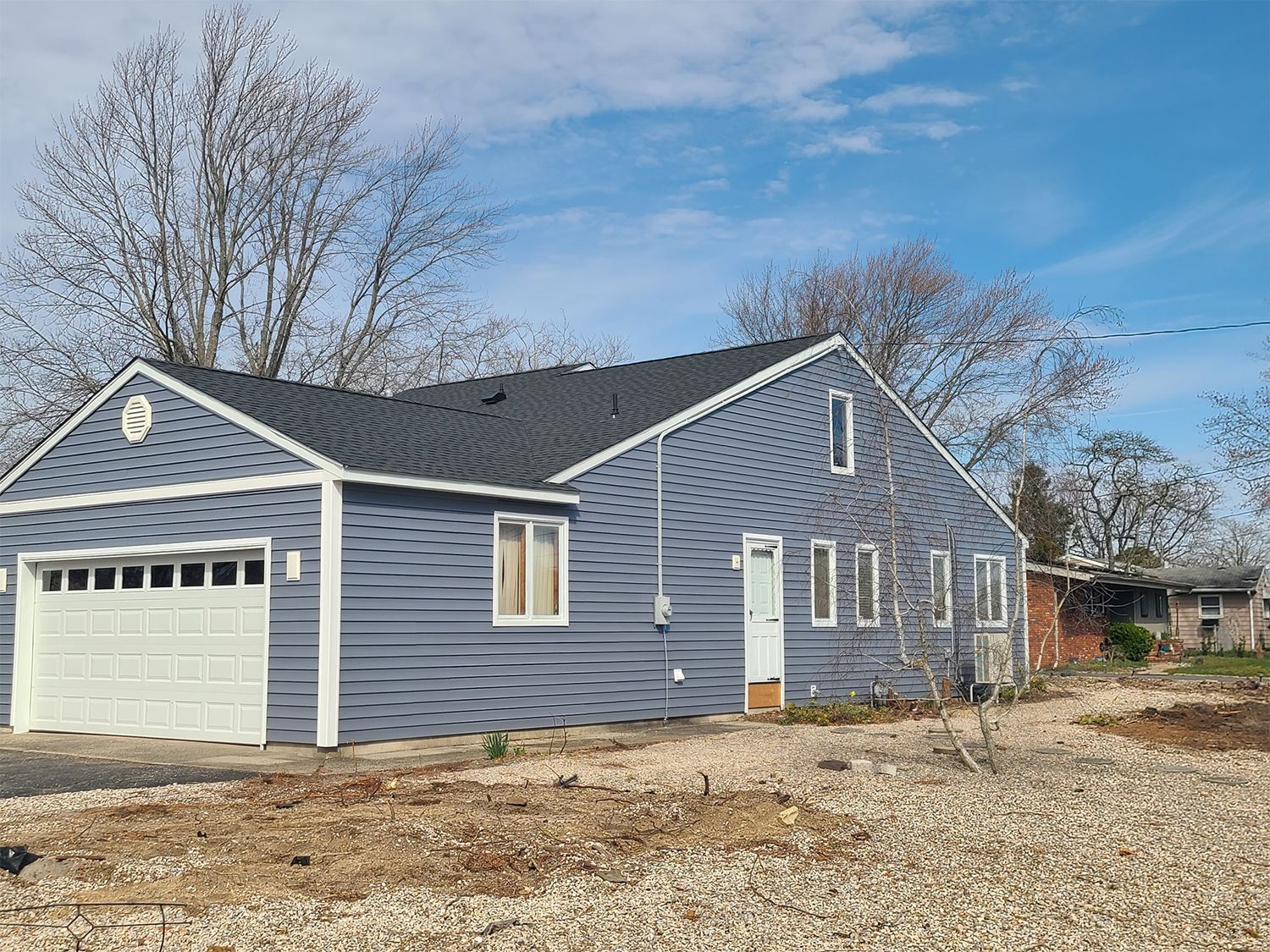 A gray house with a white garage door is sitting on top of a gravel lot.
