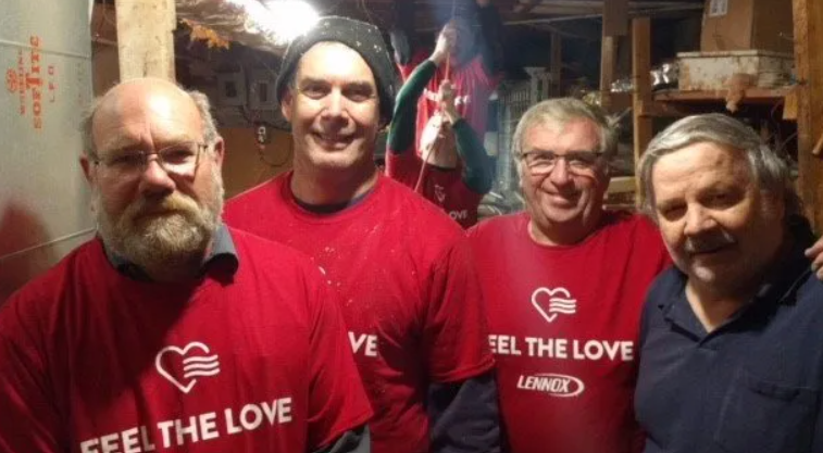 Four people in red “Feel the Love” shirts smiling indoors in a warmly lit room
