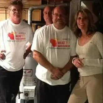 Four people in white T-shirts pose in a basement utility room beside a water heater.