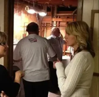 People standing in a narrow indoor hallway with warm lighting, one person in a white sweater in the foreground