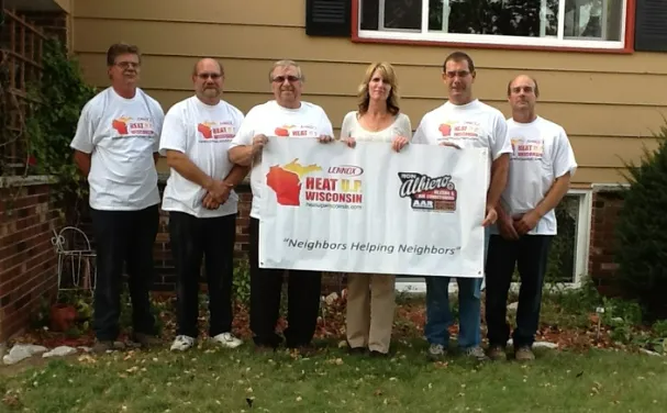 Six people in white shirts holding a banner at a Breast Cancer Awareness event outdoors