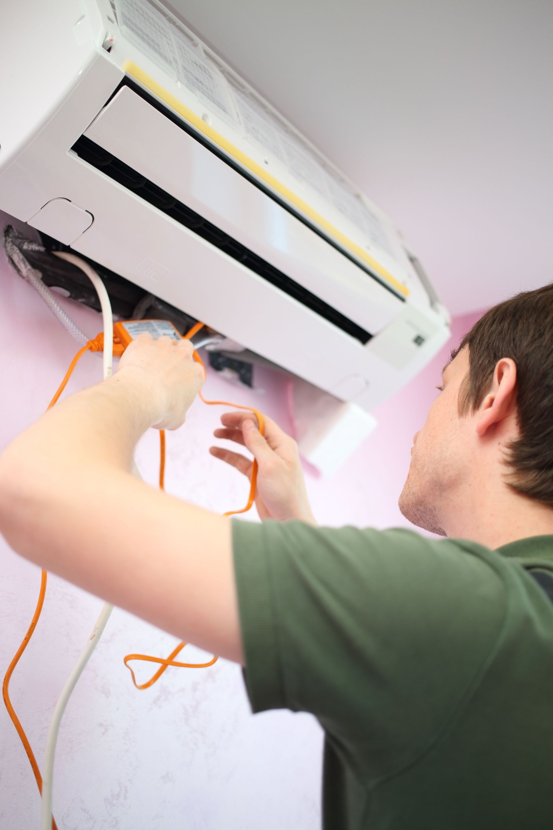 Technician installing an air conditioner on a wall, holding orange wires.