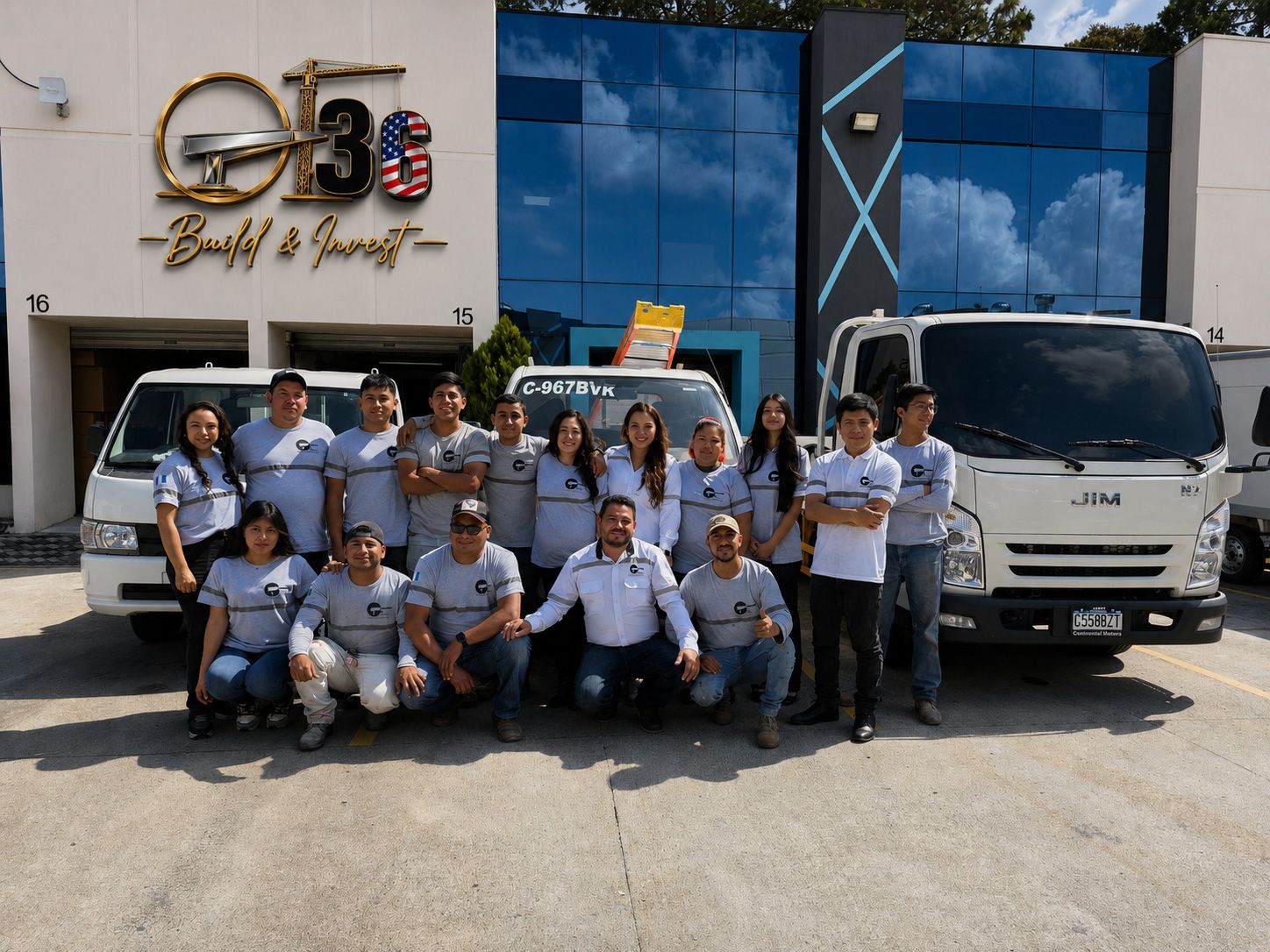 Group of employees posing in front of a blue building and company trucks in bright sunlight
