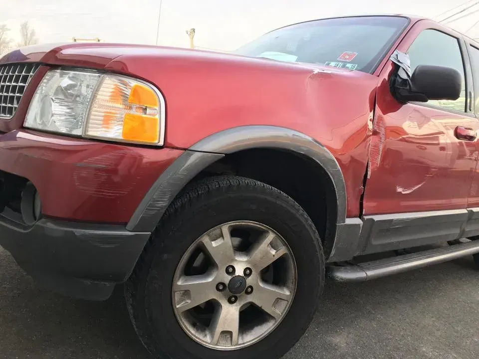 Red pickup truck with front left damage, parked outdoors on a roadside.
