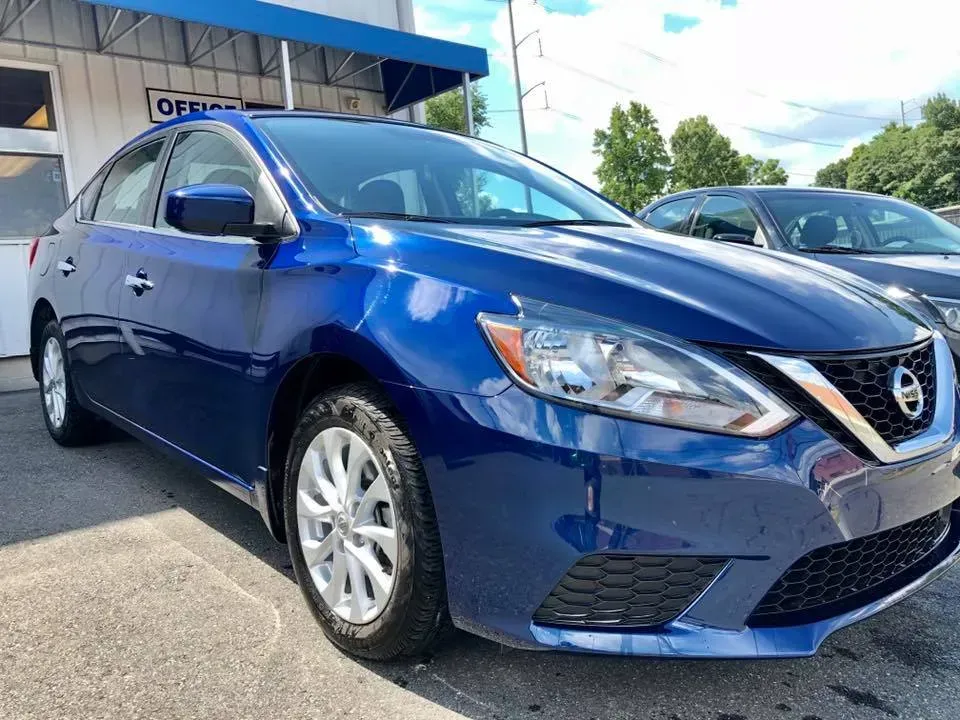 Blue Nissan sedan parked outside a dealership on a sunny day