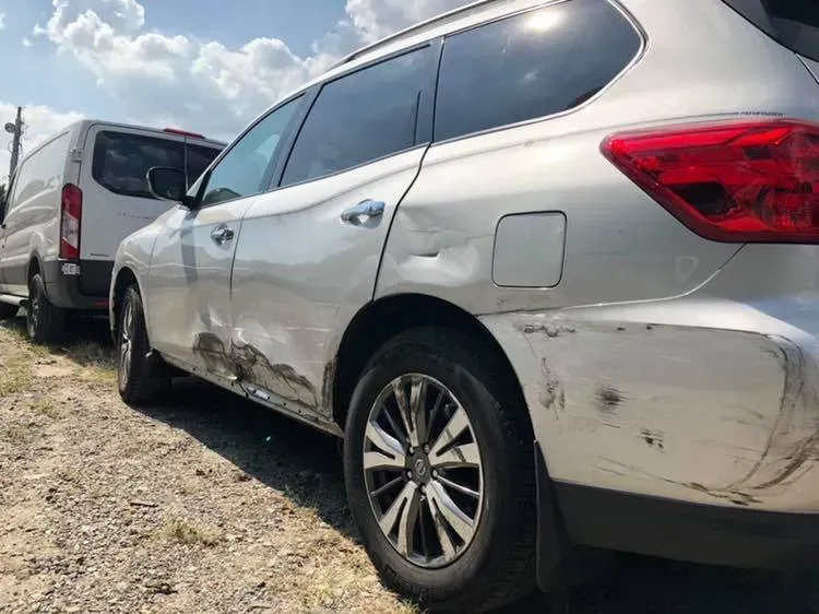 Silver SUV with side and rear damage parked beside a white van on a gravel lot