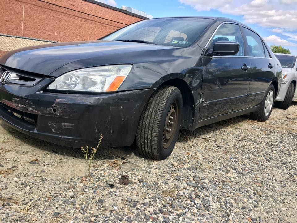 Black sedan parked on gravel beside a brick building, front-left view.
