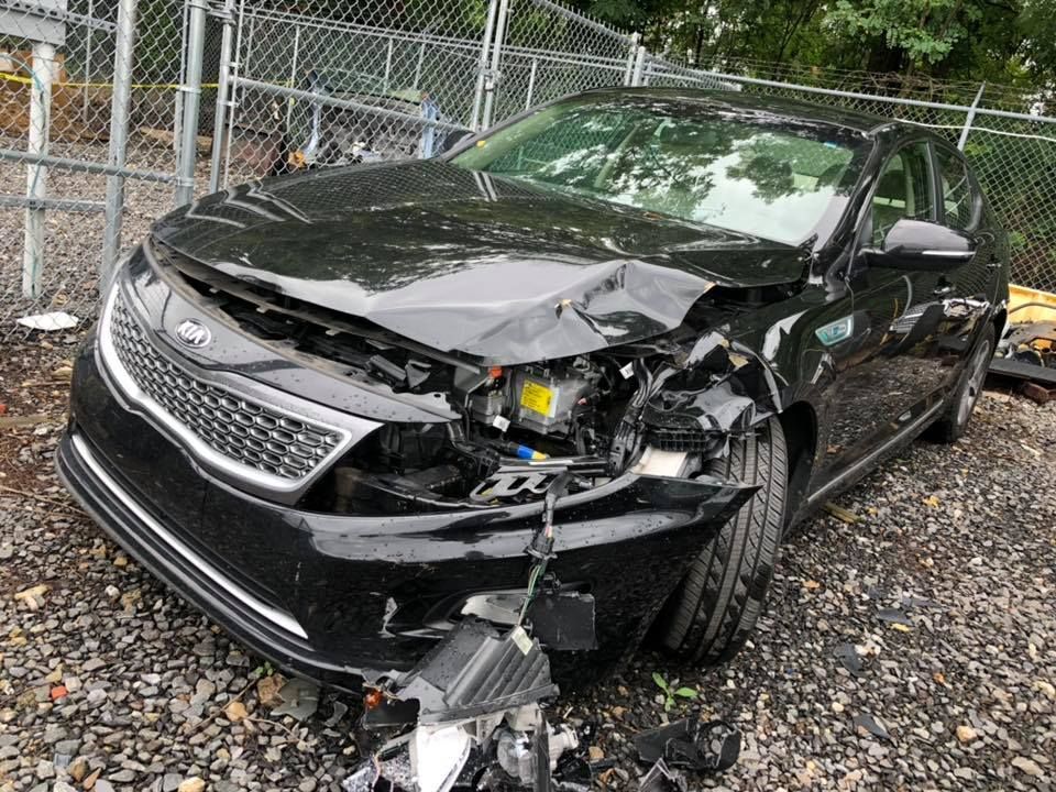 Black sedan with severe front-end damage parked by a chain-link fence