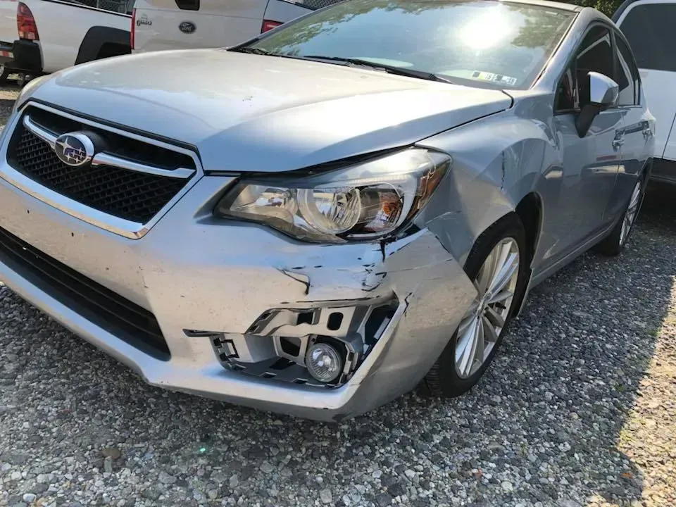 Blue Subaru sedan with front-right bumper damage in a gravel lot