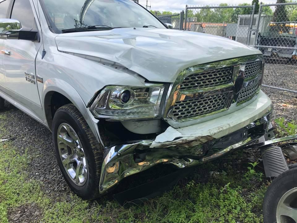 Silver pickup truck with severe front-end damage in a grassy lot near a chain-link fence