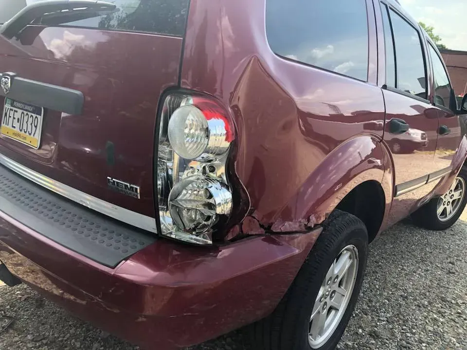 Maroon SUV with rear bumper damage and cracked left taillight, parked outdoors.