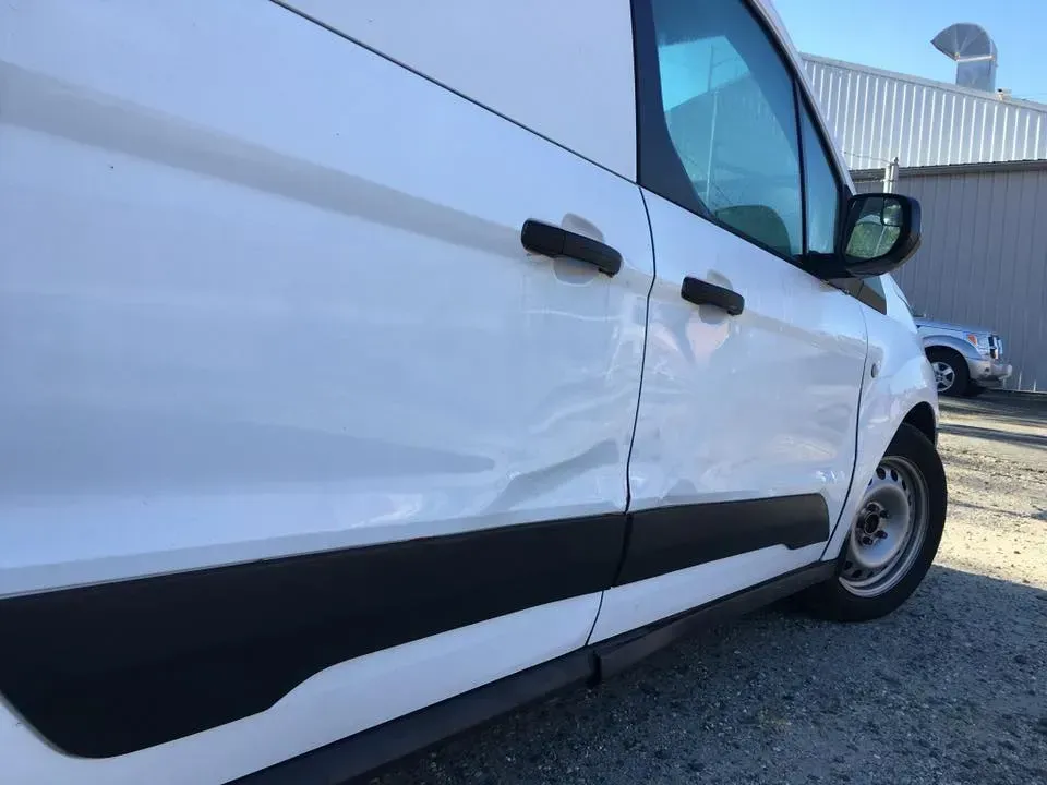 White van with black trim parked outdoors on gravel near a building