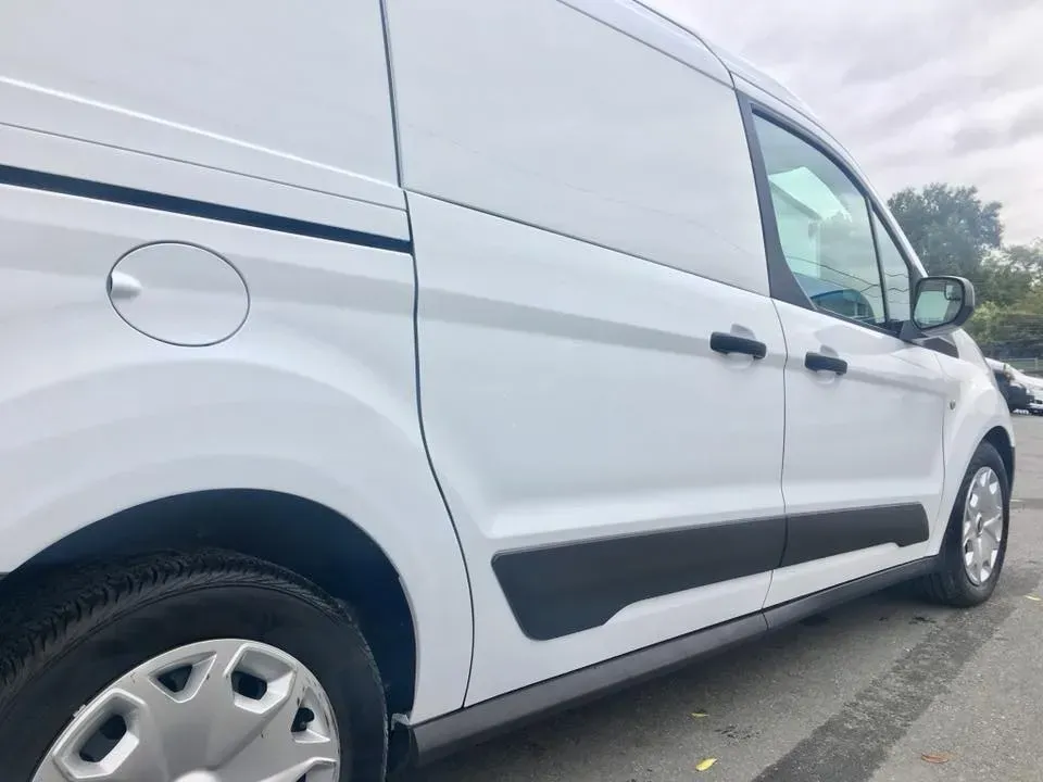 White cargo van parked on a roadside, side view with black trim and cloudy sky.