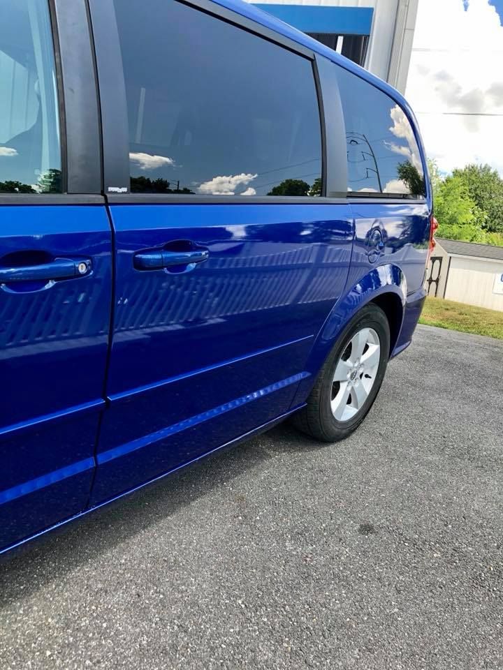 Blue minivan parked on a paved lot beside grass under a partly cloudy sky