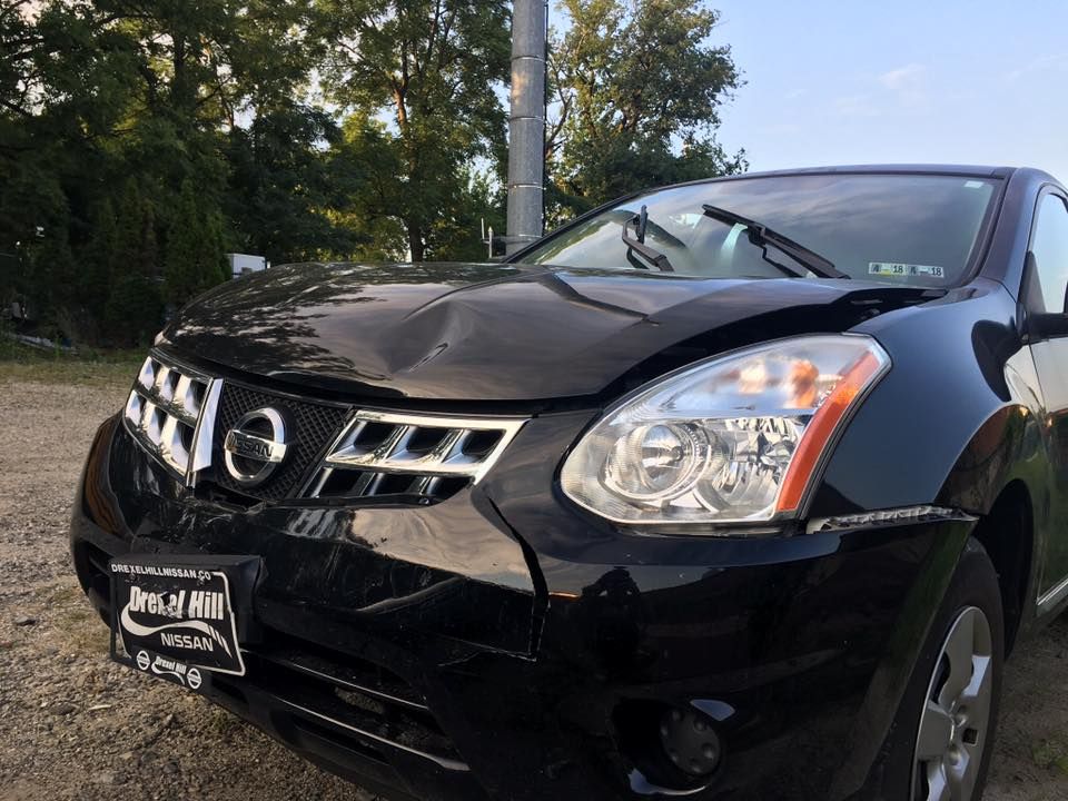 Black Nissan sedan parked outdoors, front view with trees in the background