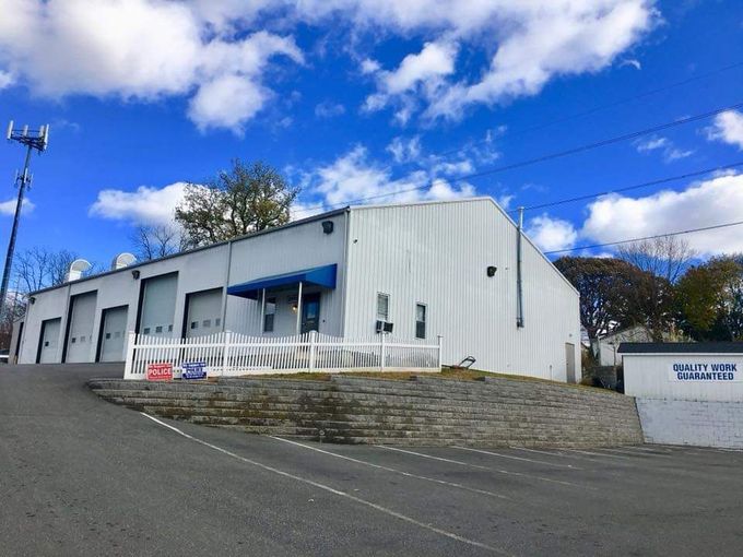 White industrial building with blue awnings on a sloped street under a bright blue sky