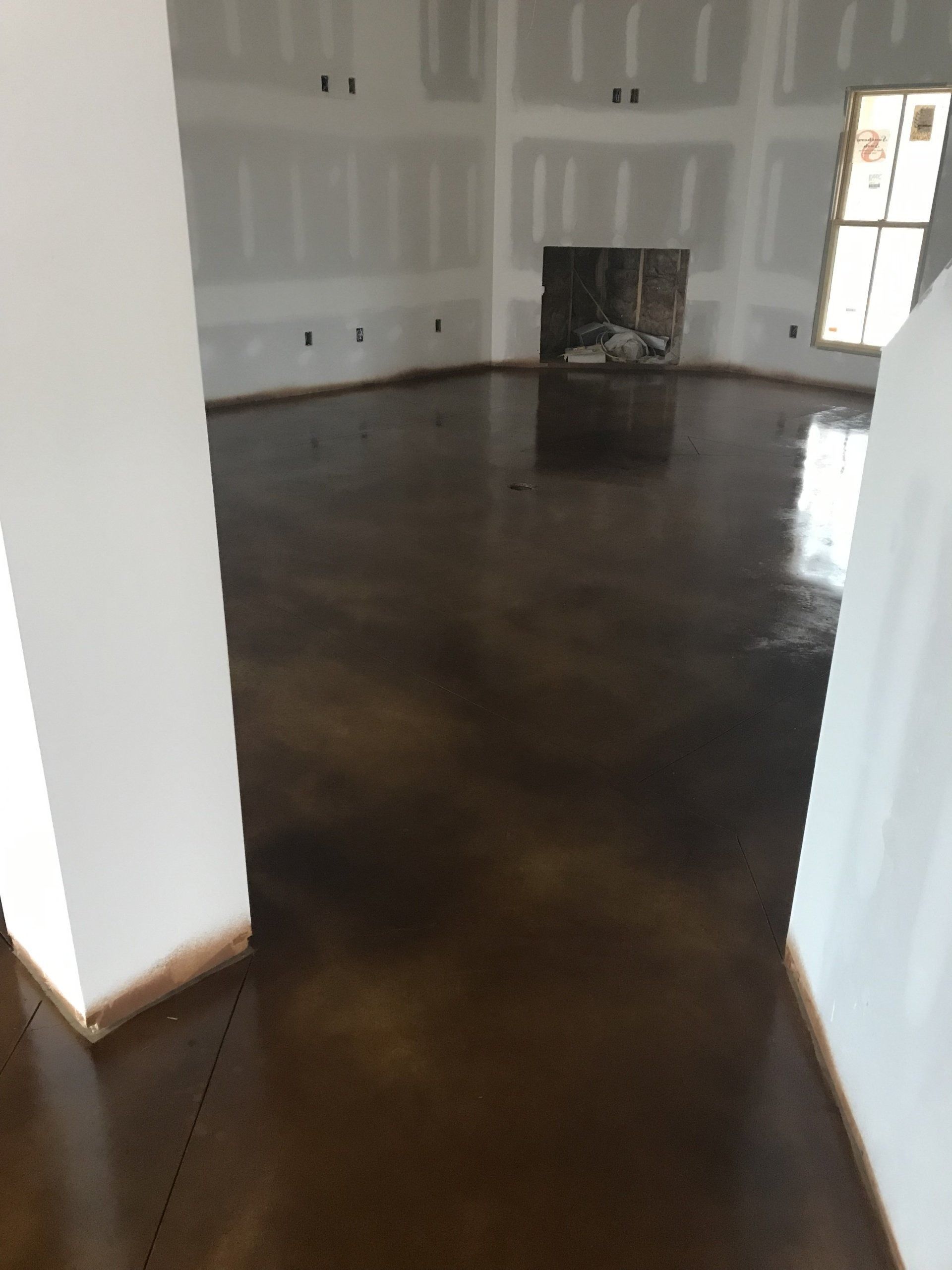 Brown stained concrete floor in a room with white walls and a fireplace.