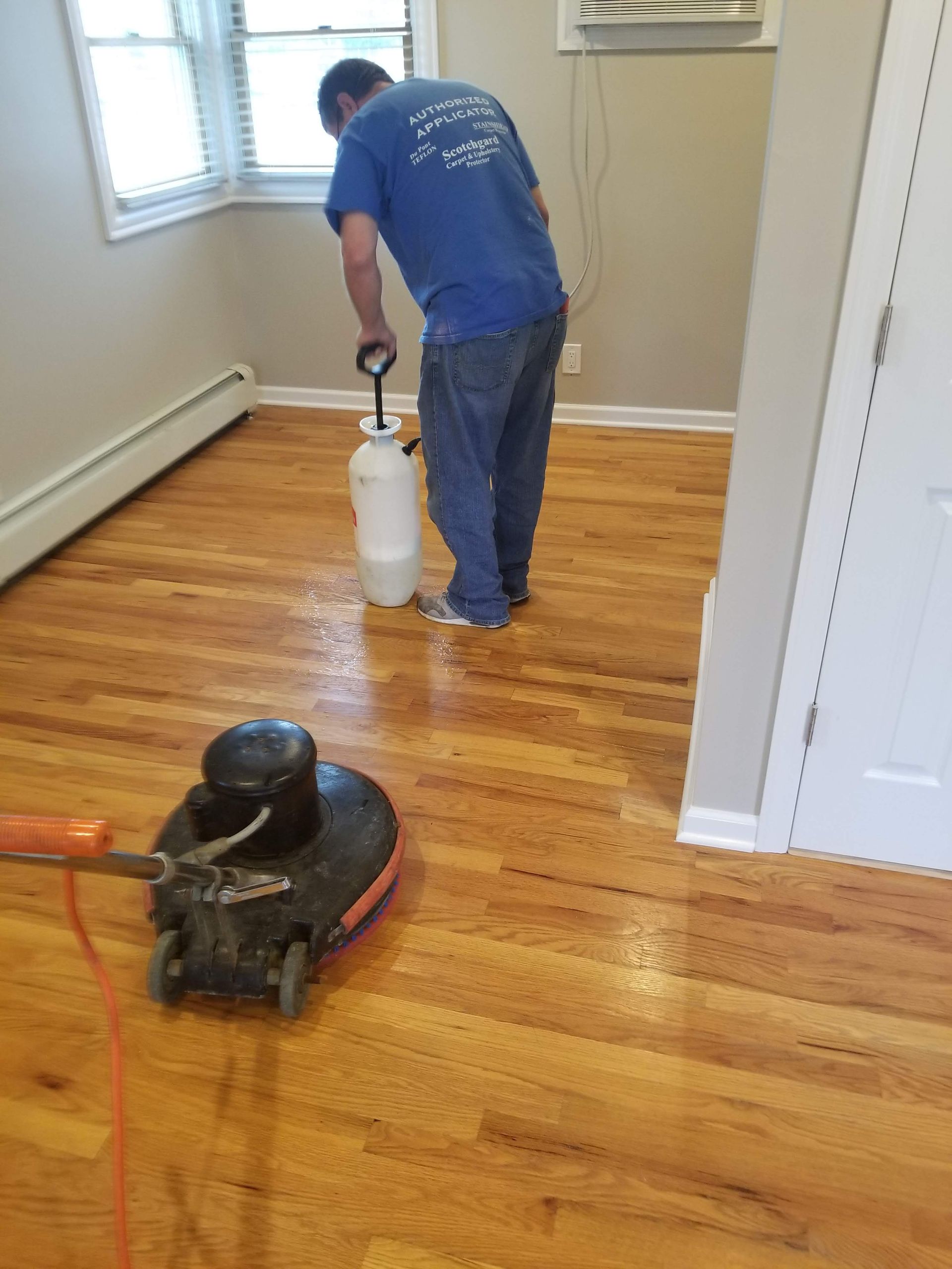 Man polishing a hardwood floor with a floor buffer in a small room.