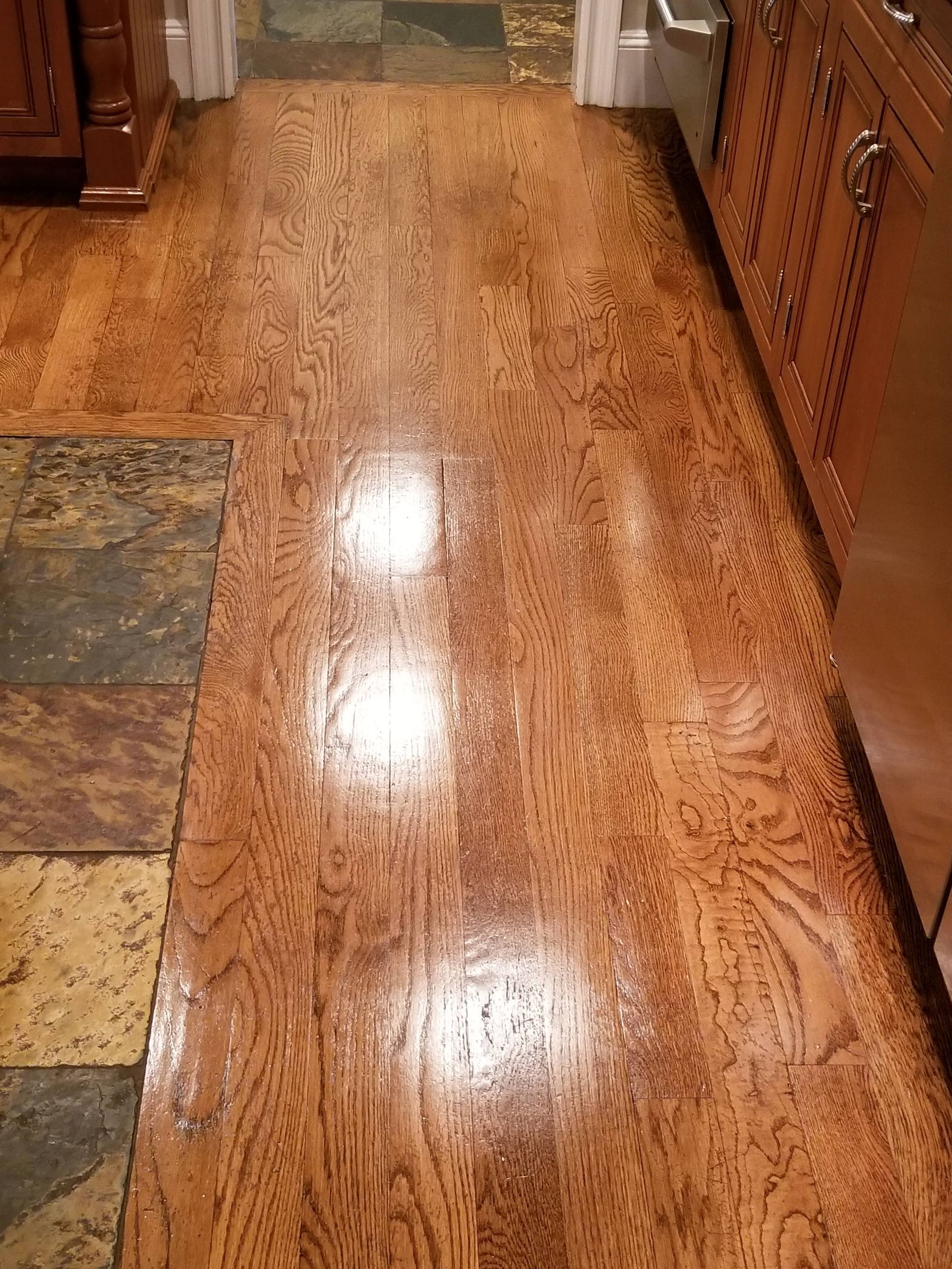 Shiny hardwood floor in a hallway with patterned tile edges and wooden cabinets on both sides