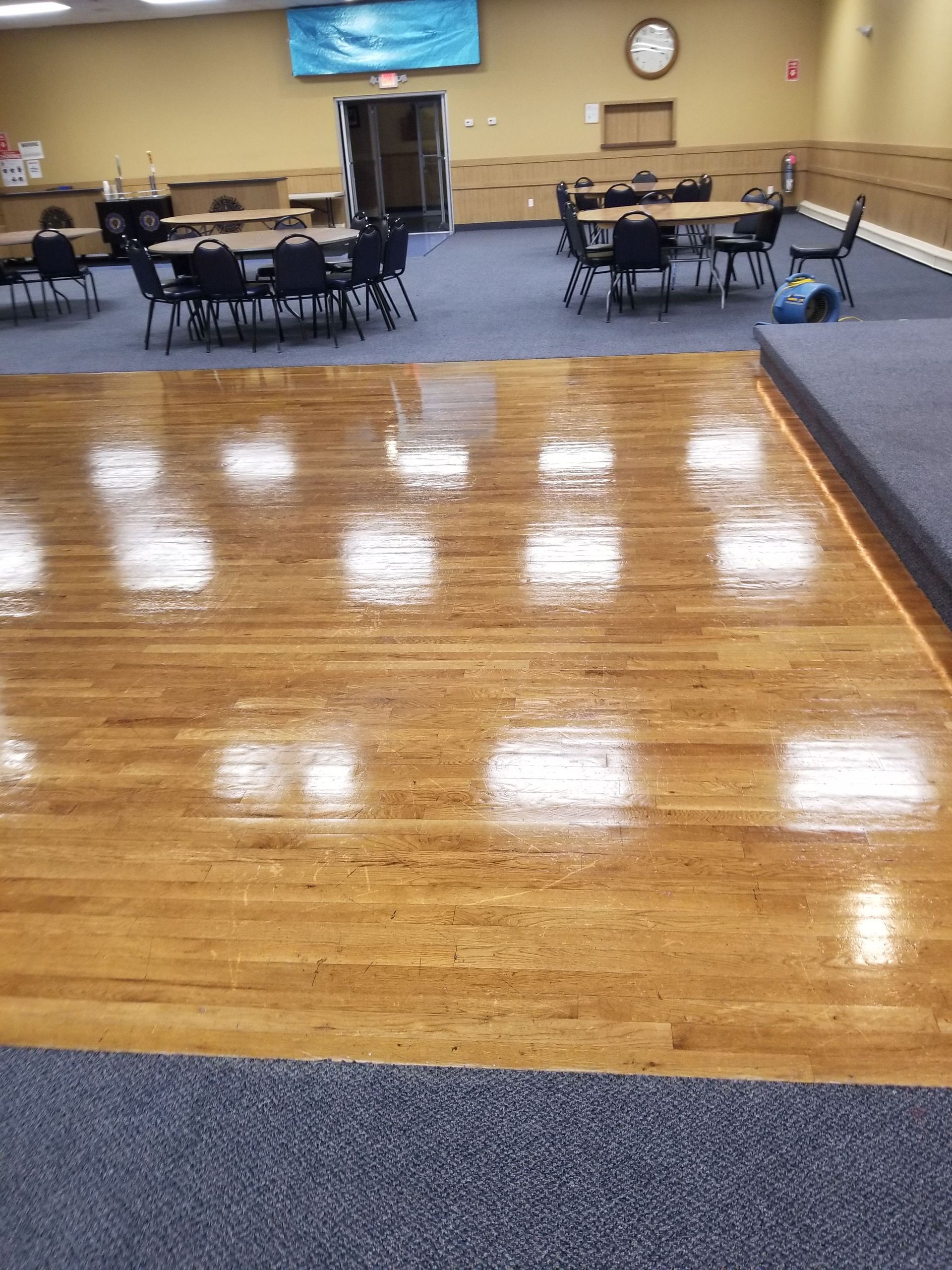 Community hall with shiny wooden floor, round tables and chairs, and a low stage in the background