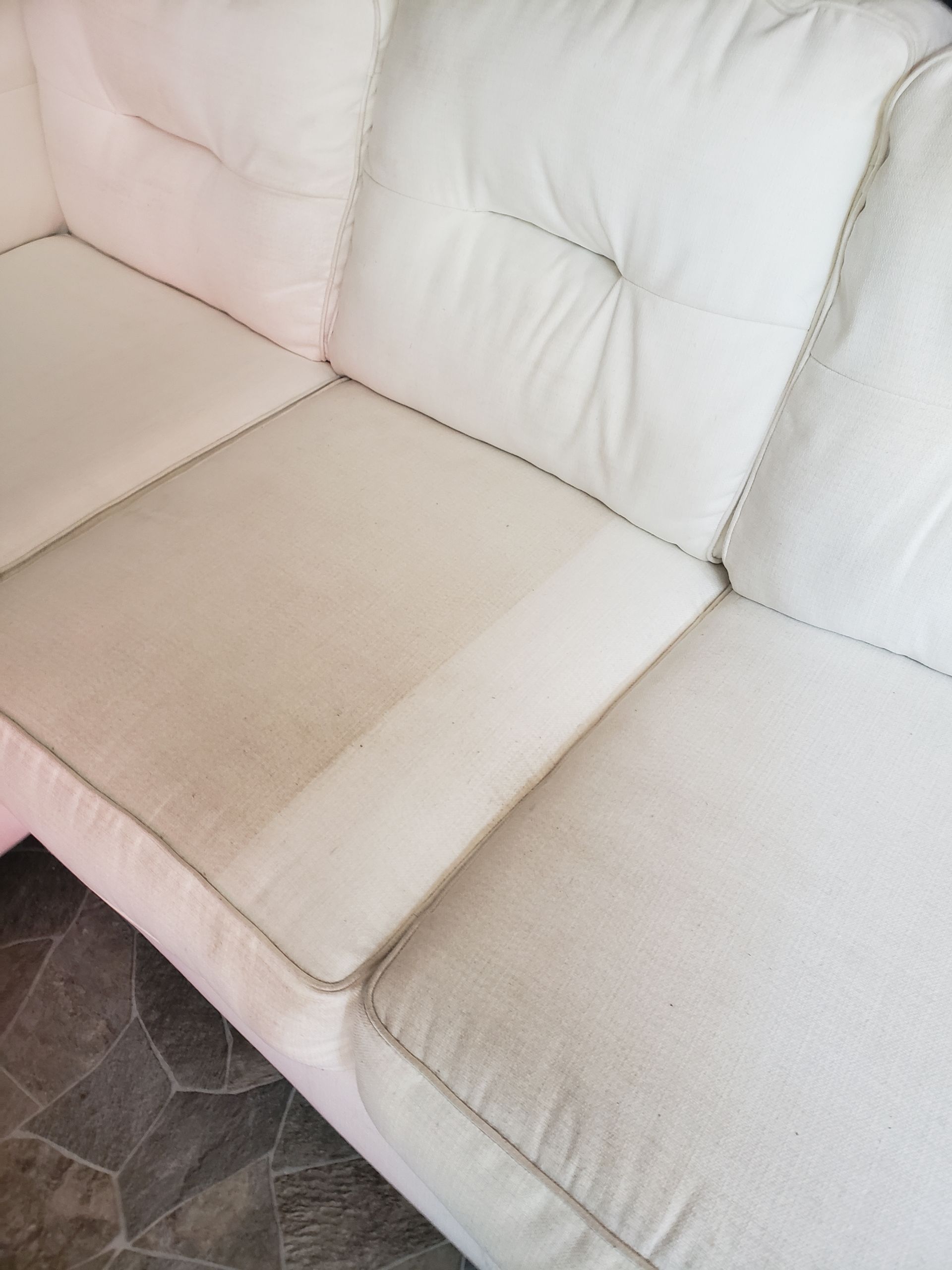 White cushioned sofa in a corner, with beige carpet and a tiled floor nearby.
