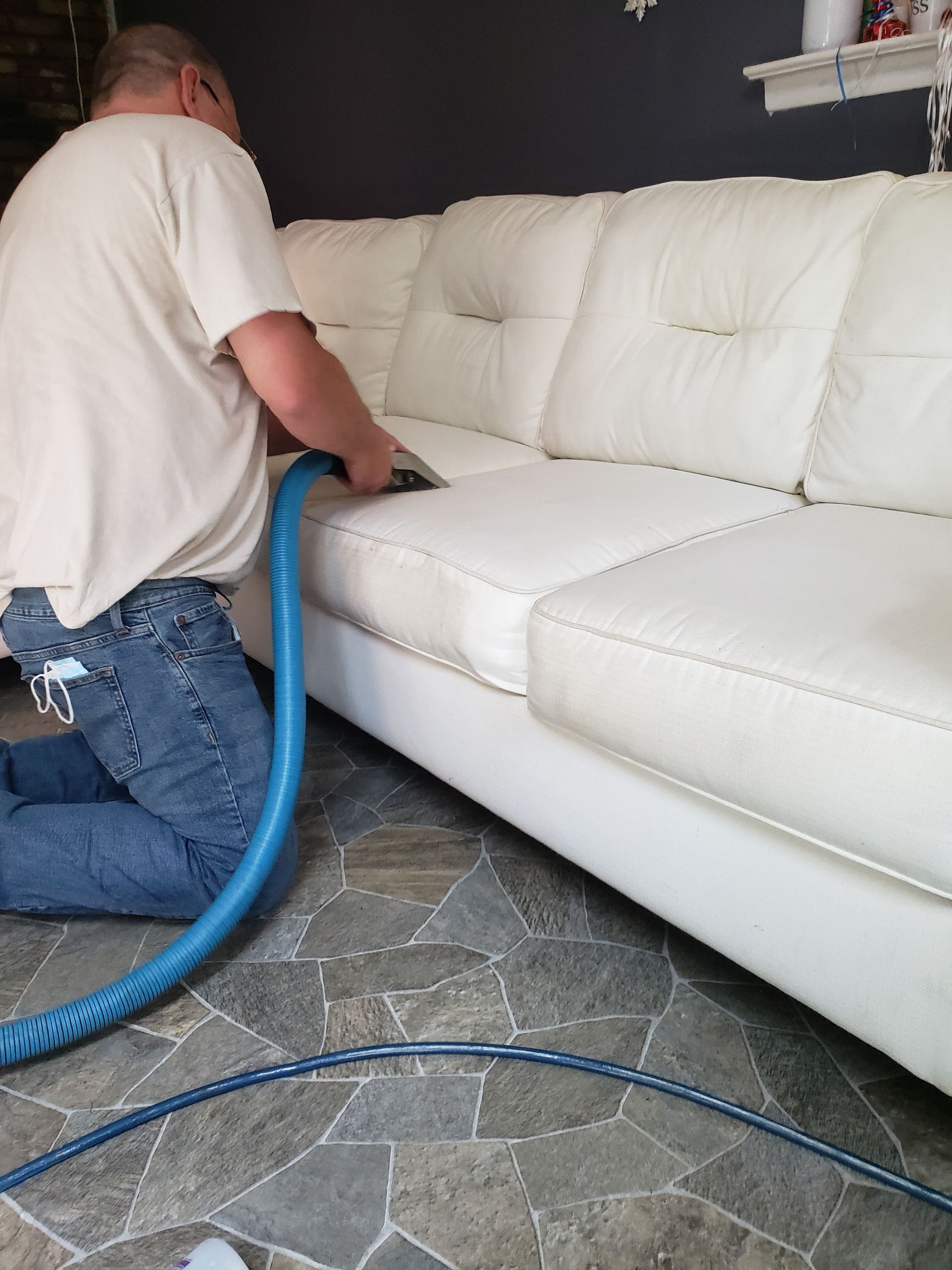 Technician vacuuming a white sofa in a living room with a blue hose