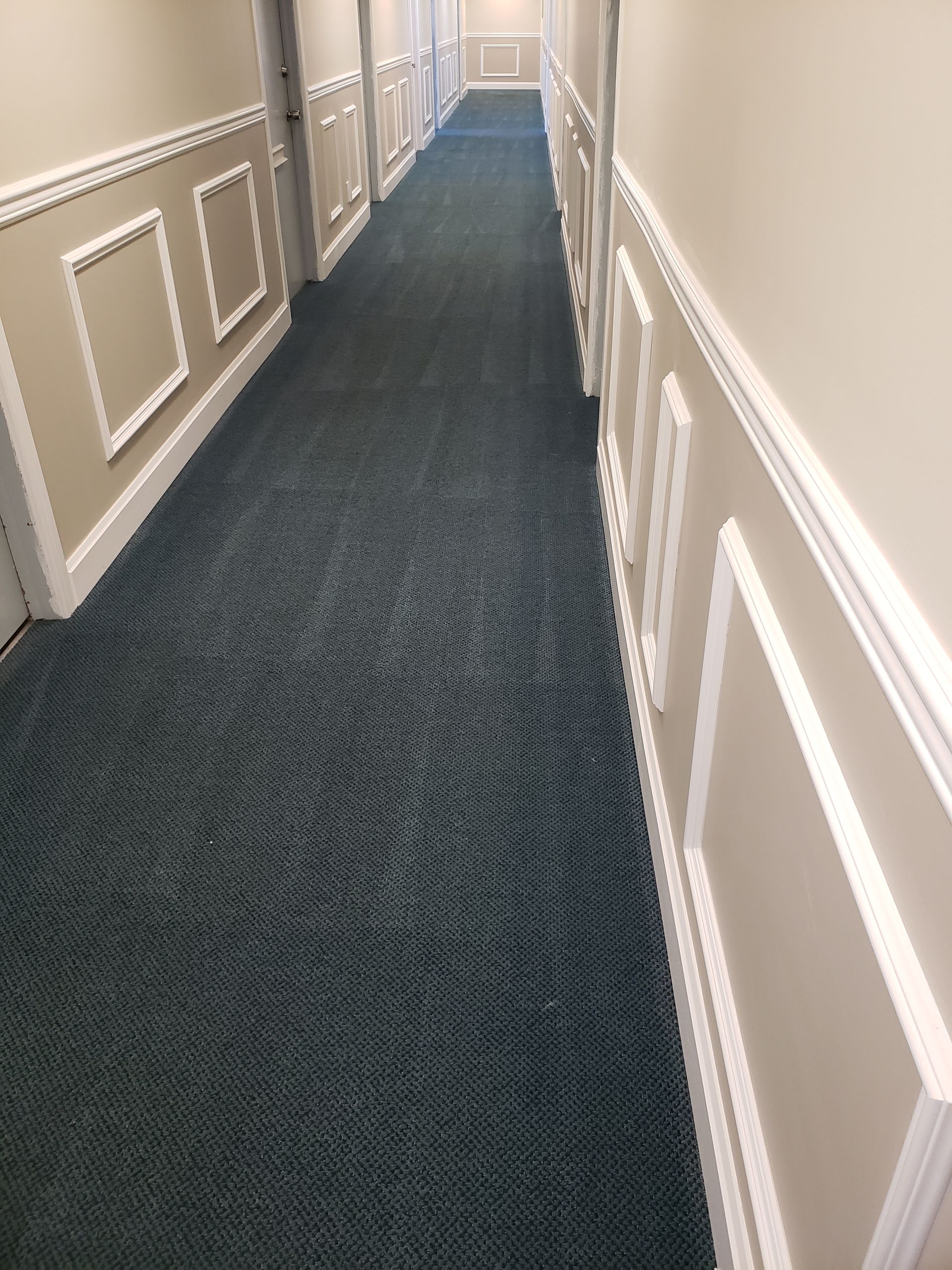 Long hotel hallway with beige paneled walls and dark blue carpet.