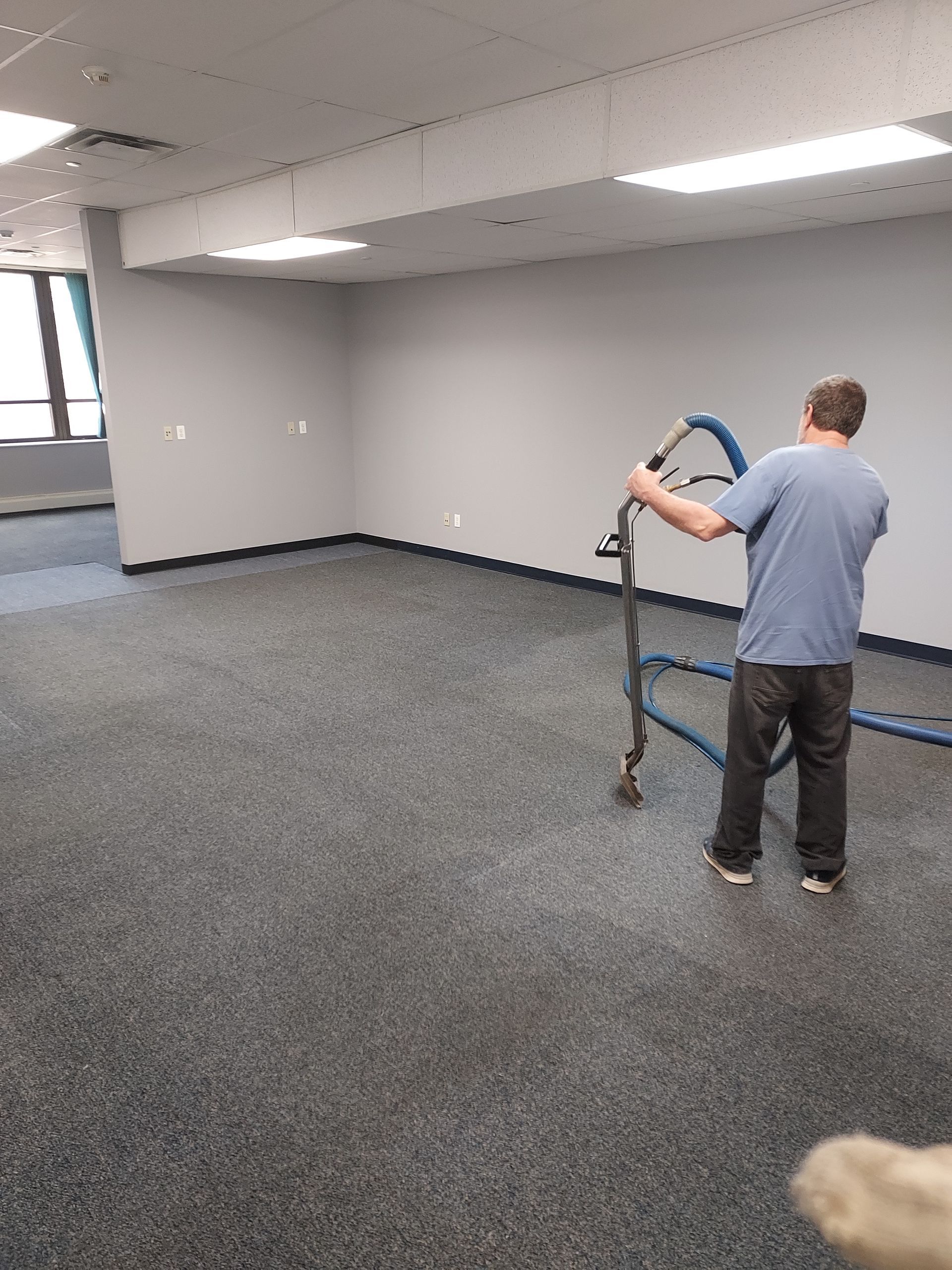Person in blue shirt moving a cart in an empty carpeted office room.