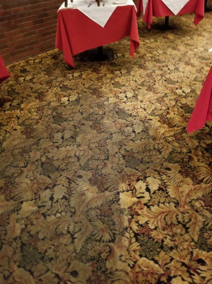 Carpeted banquet room with red-draped tables along a brick wall