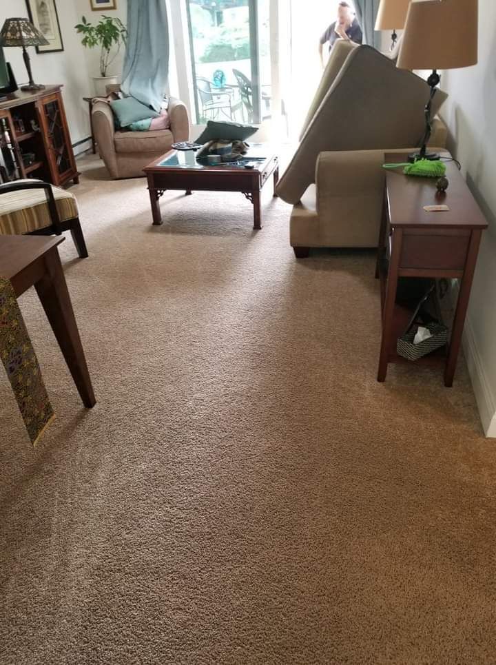Living room with beige carpet, a tipped-over armchair, coffee table, and sunlit windows.