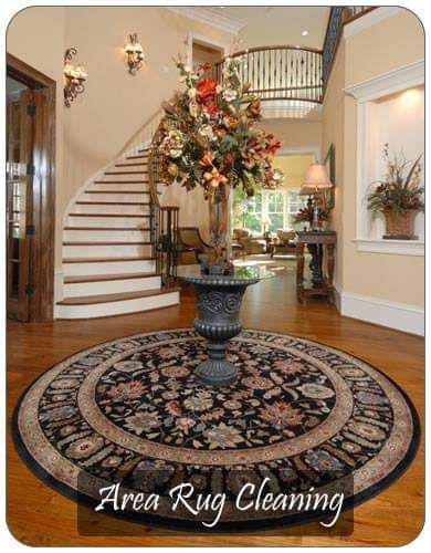 Elegant foyer with spiral staircase, floral arrangement, and round oriental rug; “Area Rug Cleaning” text at bottom