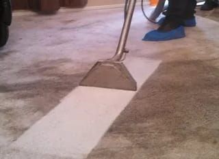 A floor-cleaning tool with a blue handle beside a white painted strip on a concrete floor.