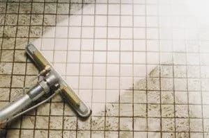 A shower squeegee on a tiled floor with dirty water stains and grime.