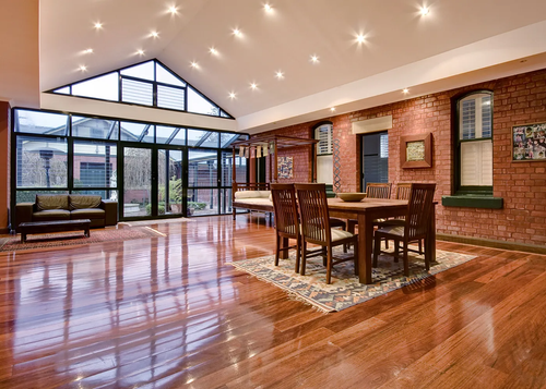 Spacious dining room with wooden floor, brick walls, and glass wall leading to a small patio.