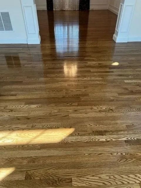 Hardwood floor, polished and reflecting sunlight, in a room with white trim.