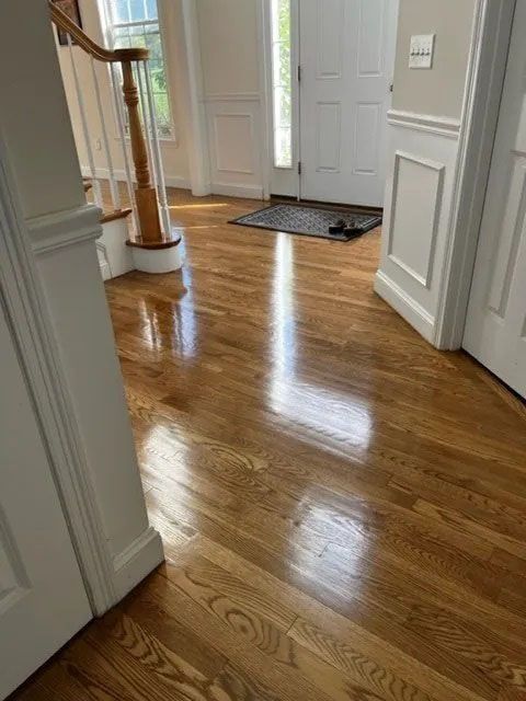 Polished hardwood floor in an entryway with white wainscoting, a staircase, and an open door.