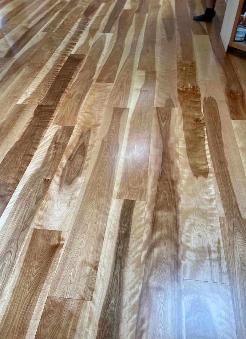 Wood floor with wavy edges, varying light brown hues, reflecting light.