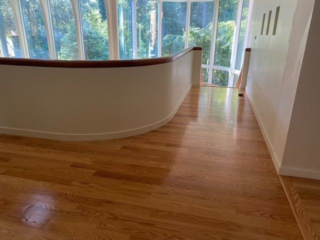 Hardwood floor and white curved wall with a wooden railing, near a large window.