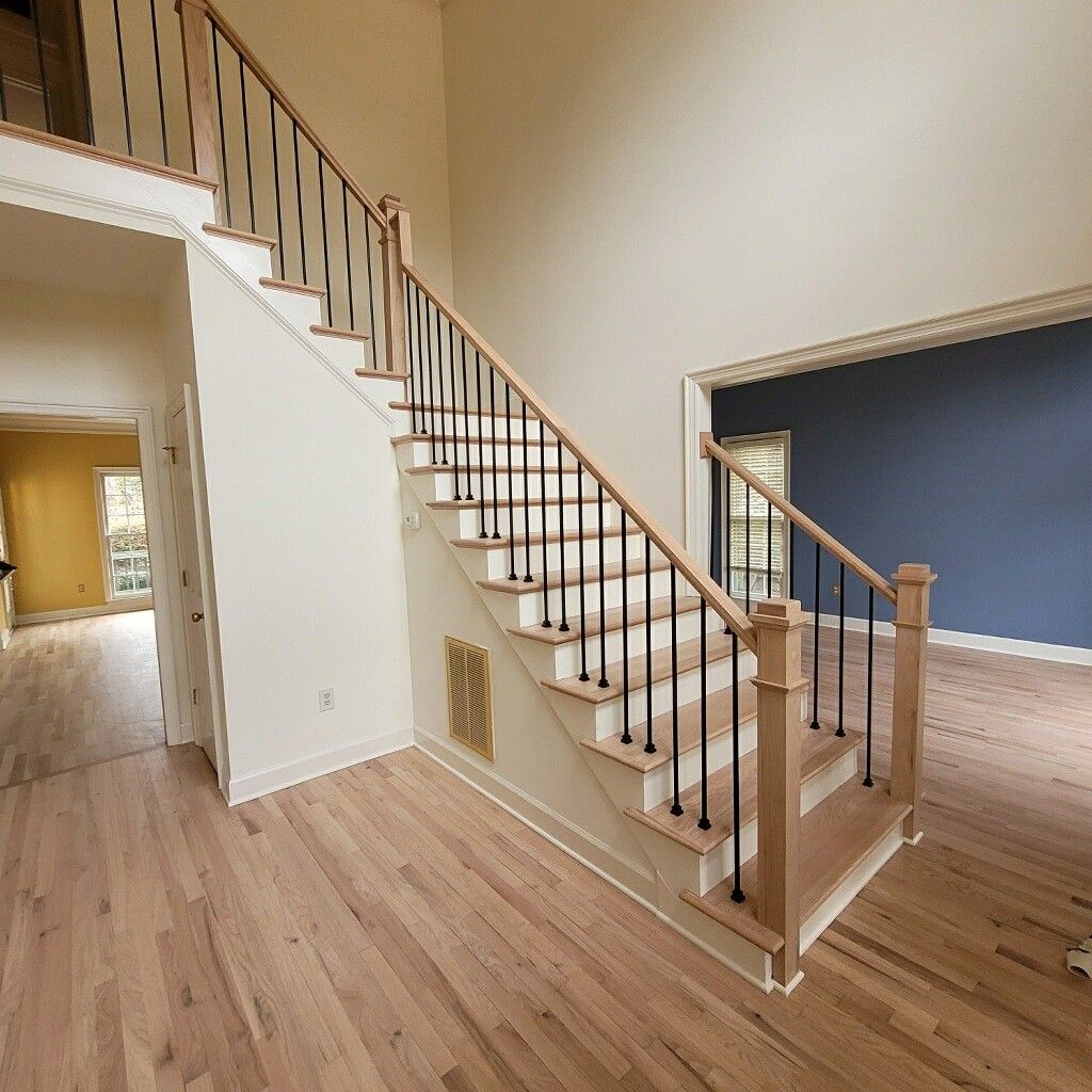Staircase with light wood steps and black iron balusters in a brightly lit entryway with light wood floors