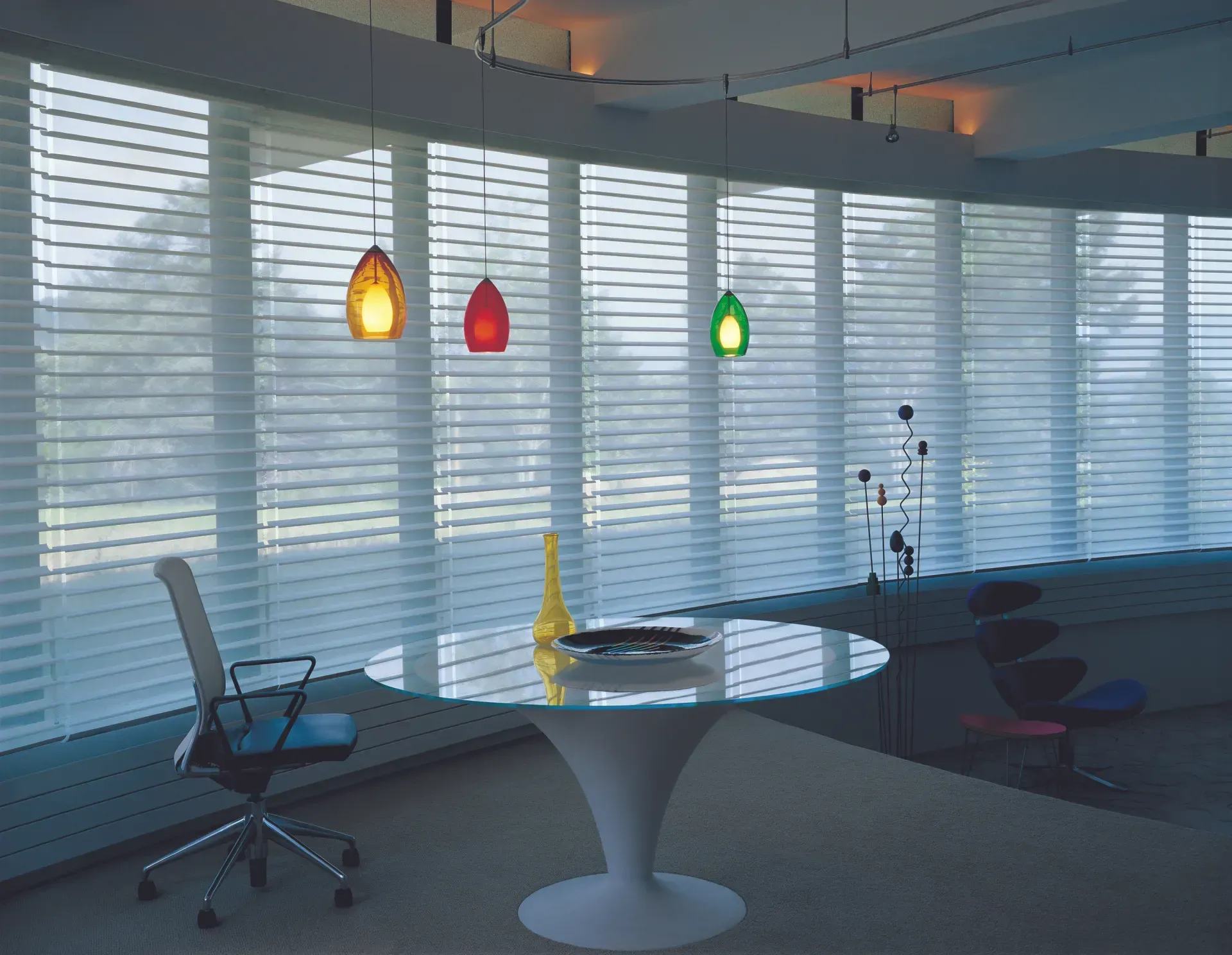A room with a table and a chair in front of a window with blinds