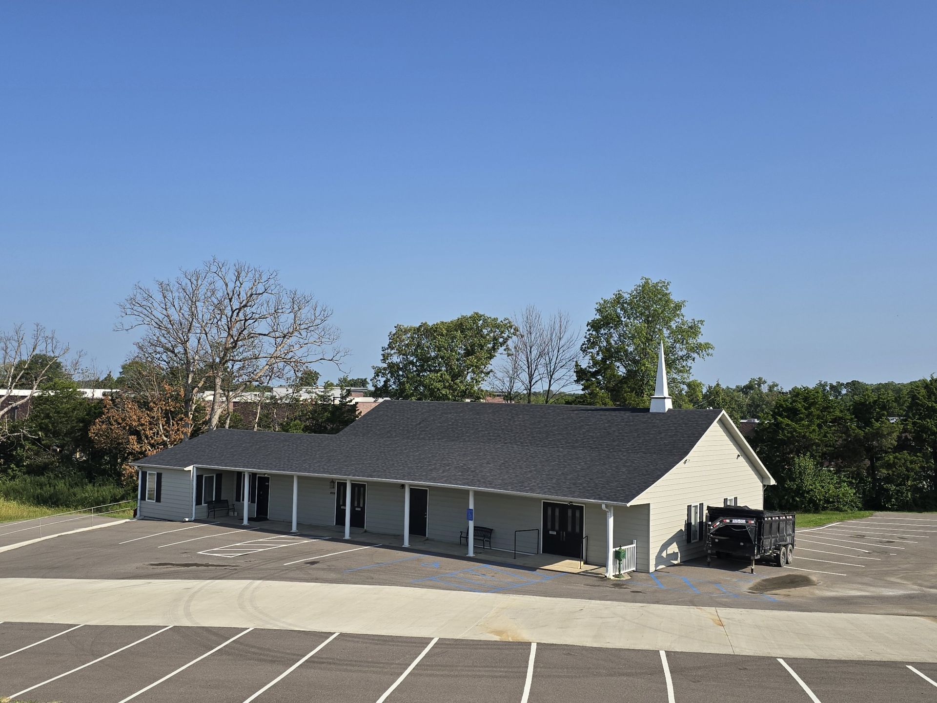 A white building with a black roof is in a parking lot