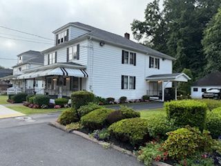 White multi-story building with black shutters, awnings, and landscaped yard.